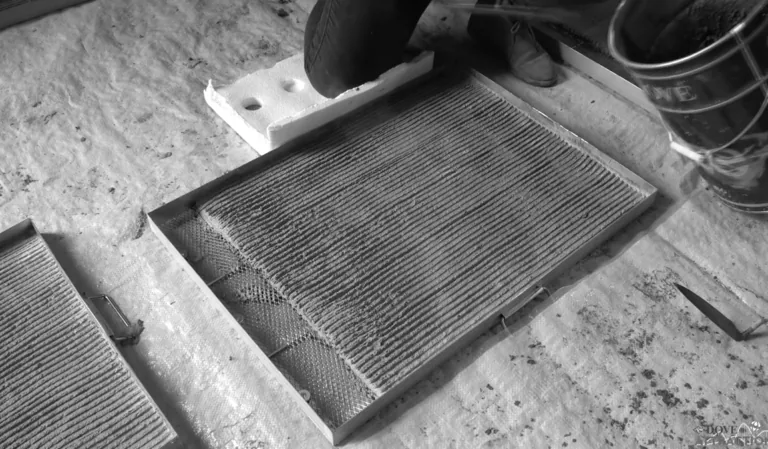 A person applies a scratch coat of cement to a metal lath tray on a drop cloth.